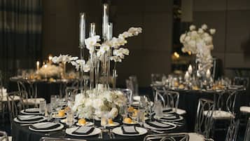 A formal dining setup with tables set for multiple guests, featuring clear glassware, white flowers, and candles.