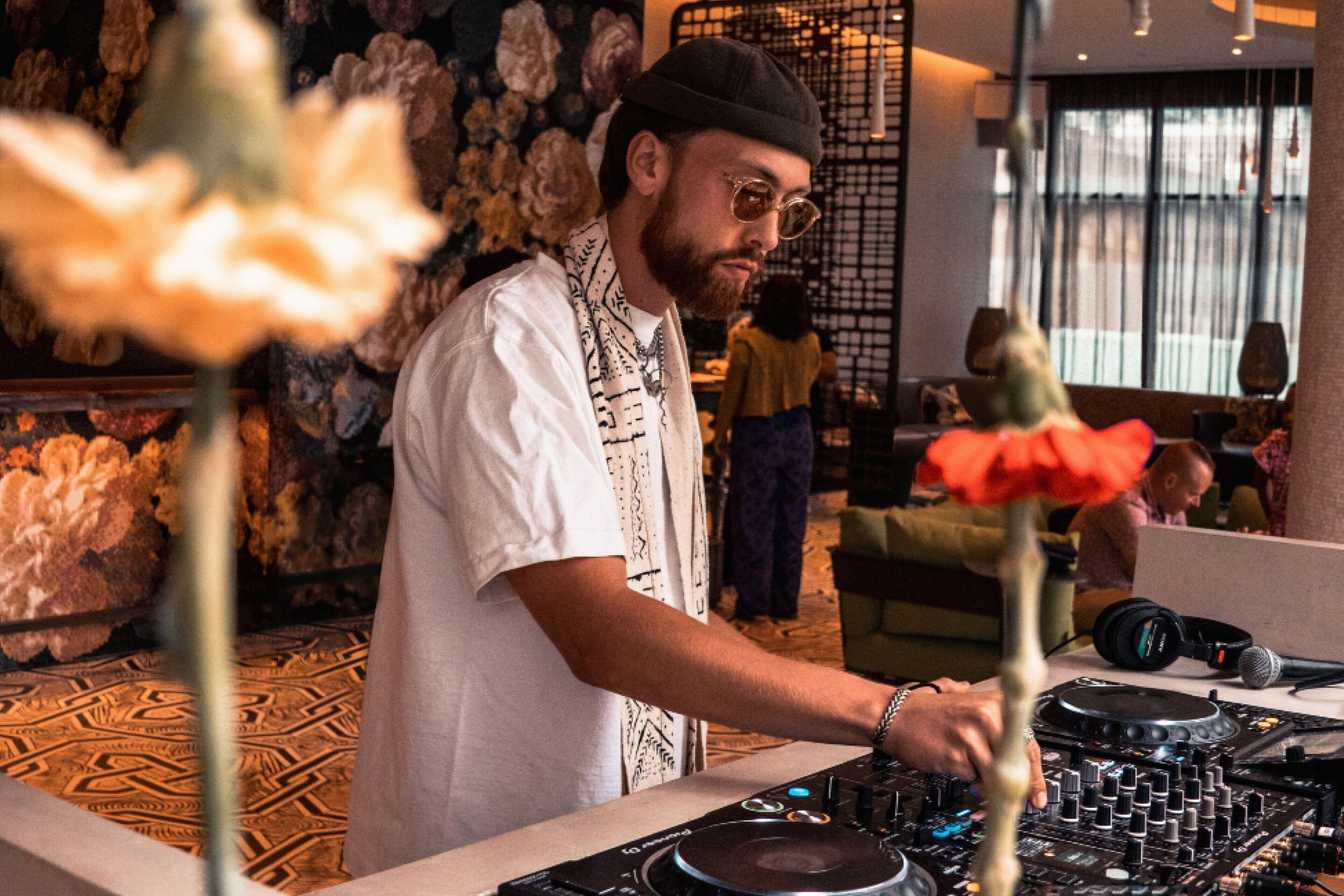 A person operating DJ equipment in a room with patterned carpet and a decorative wall.