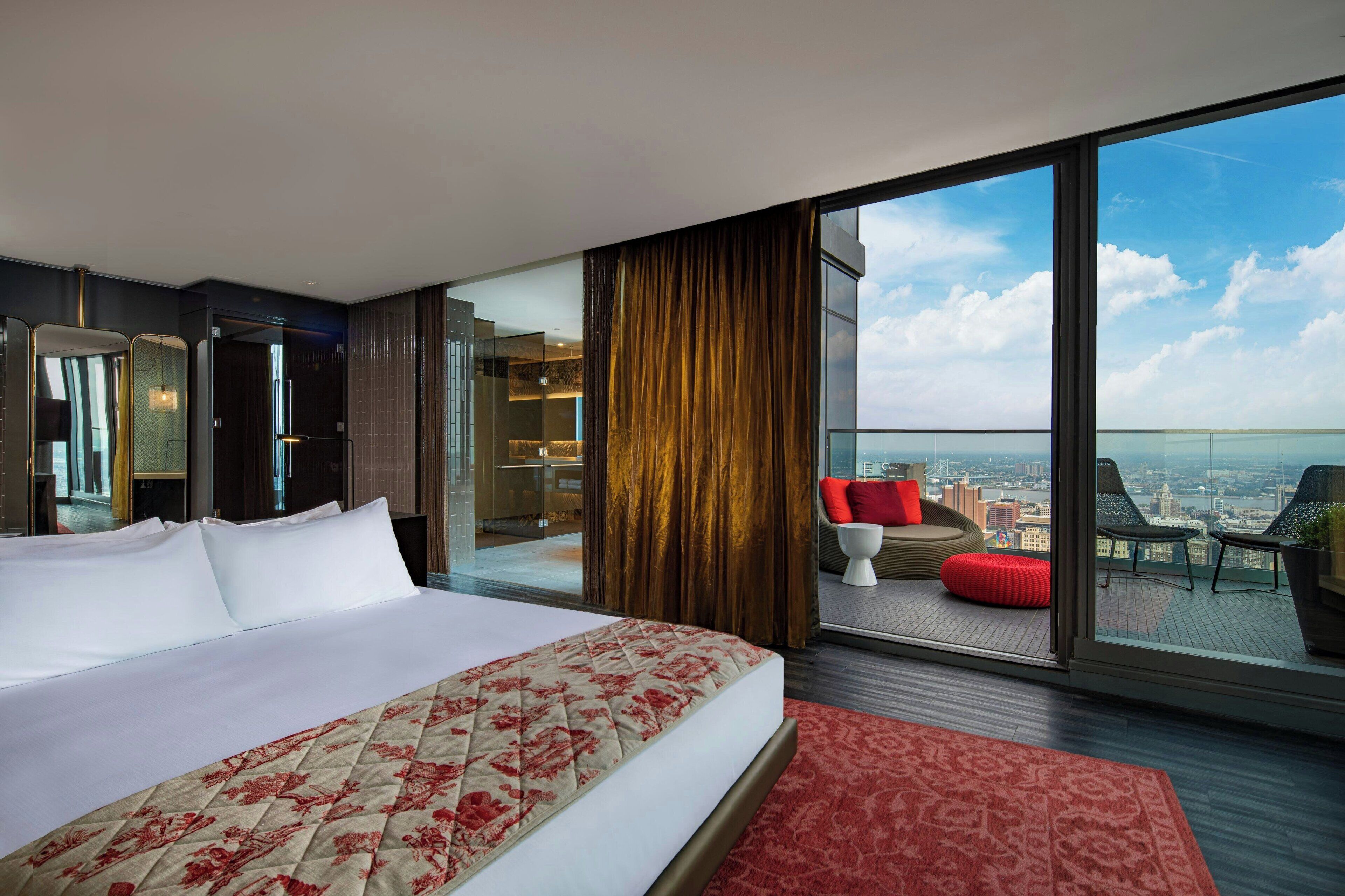 A hotel room with a large bed, a balcony with seating, and a city view.