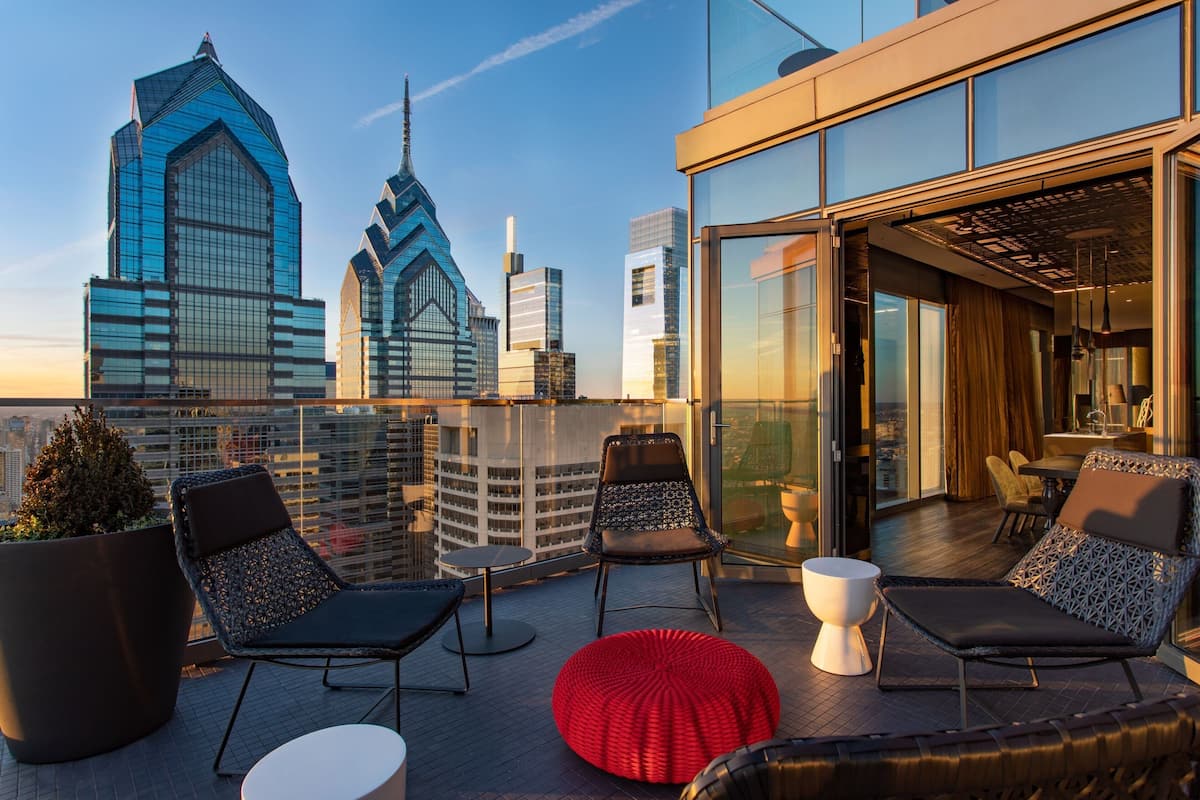 A rooftop terrace with modern seating, a large potted plant, and a city skyline view.