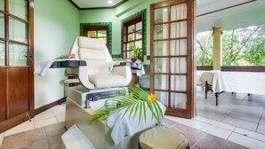 Un cuarto de spa con una silla de masaje, una mesita con una toalla y vistas al jardín a través de un ventanal.