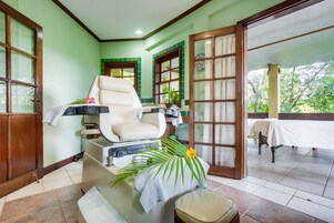 A spa room with a massage chair, a small table with a towel, and a view of the garden through a glass door.