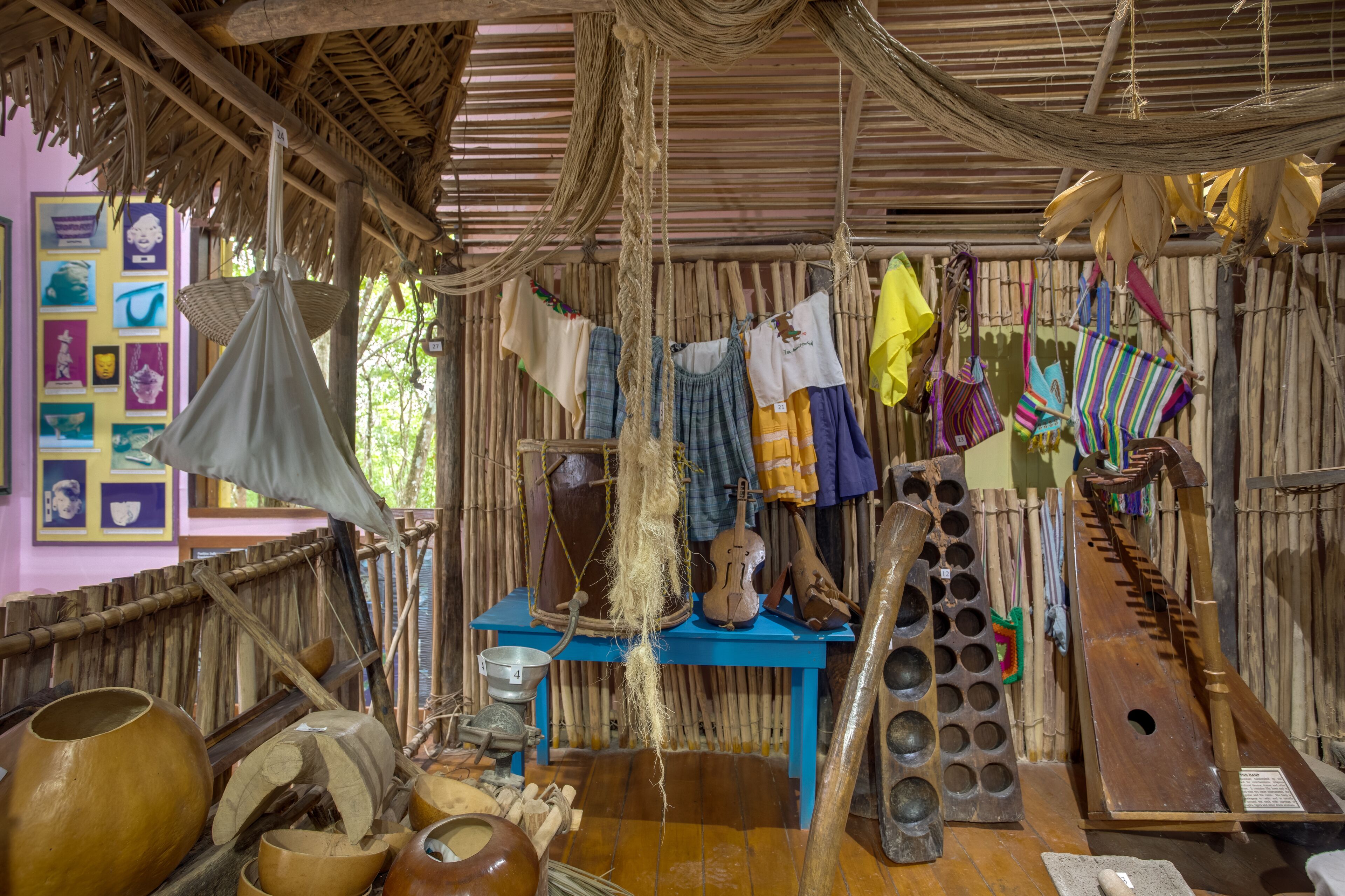 A rustic room with a thatched roof, wooden furniture, and various traditional items including pottery and woven baskets.