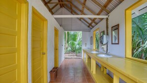 Un pasillo con puertas amarillas, piso de baldosas y un mostrador largo con lavamanos y espejos.