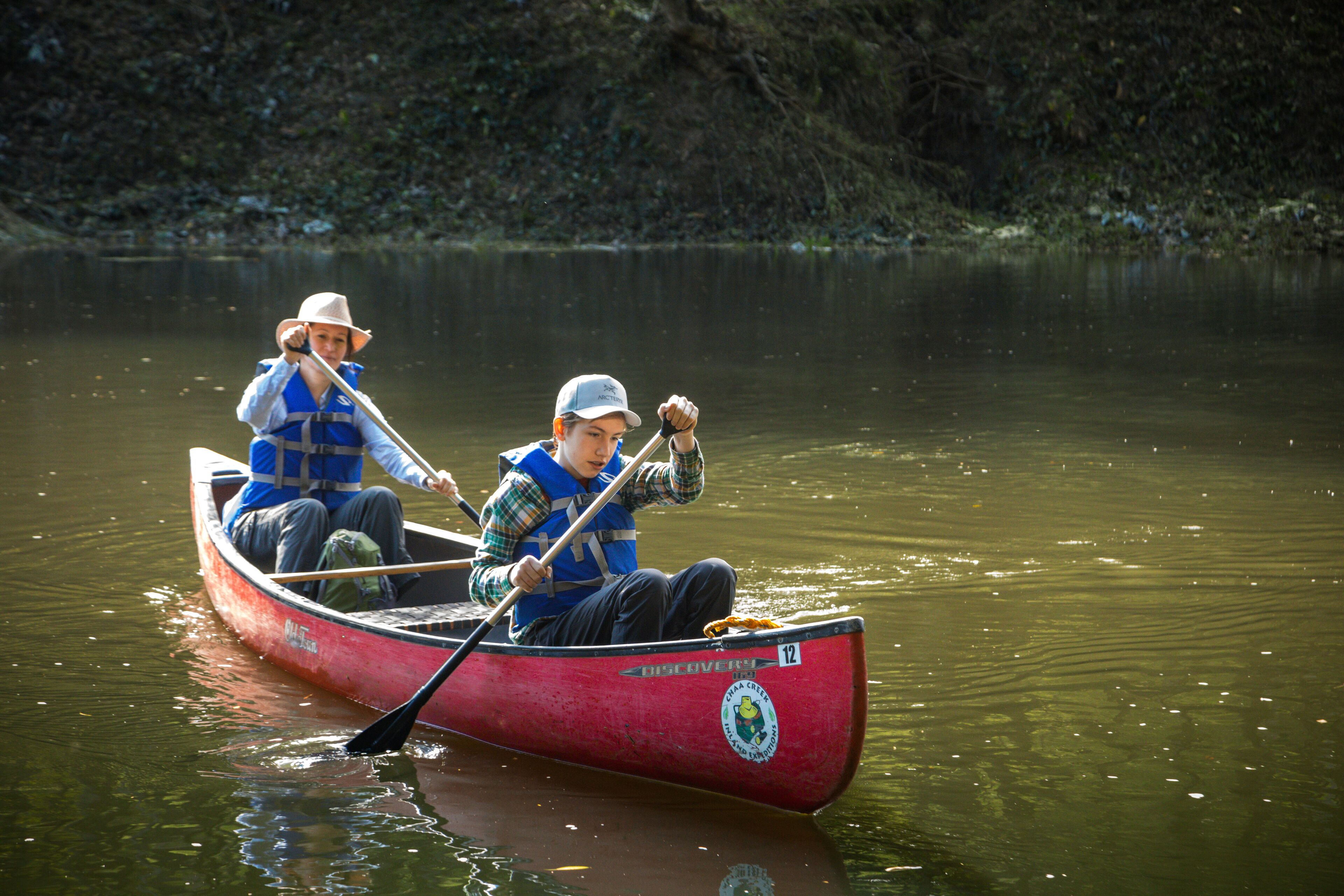 Two people in a red canoe on a calm body of water.