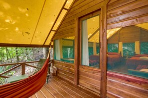 Une cabane en bois avec un hamac sur le porche, de grandes fenêtres et une vue sur la forêt.