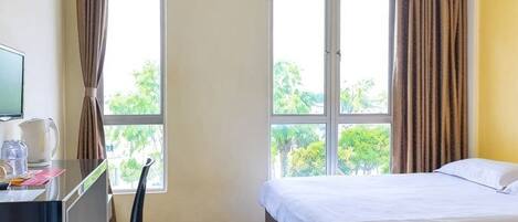 Ein Hotelzimmer mit Bett, Schreibtisch mit Stuhl, Fernseher und einem Fenster mit Vorhängen.