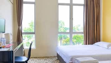 Una habitación de hotel con una cama, un escritorio con una silla, un televisor y una ventana con cortinas.