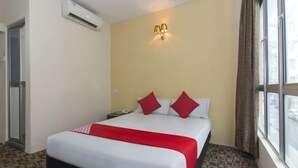 Ein Hotelzimmer mit einem Bett, einem Nachttisch, einer Klimaanlage, einem Fenster mit Vorhängen und einer Wandlampe.