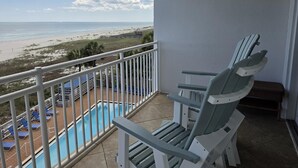 En balkong med utsikt över stranden, en pool och solstolar.