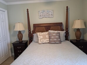 A bedroom with a large bed, two nightstands, two lamps, a door, and a wall art piece. - Cozy Gulf Front Condo in the West Building! (Pensacola)