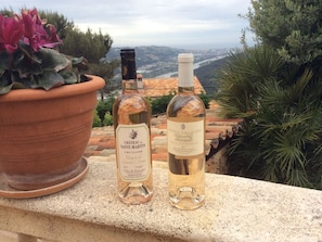 Dos botellas de vino en un balcón con una vista panorámica de un pueblo y montañas al fondo.