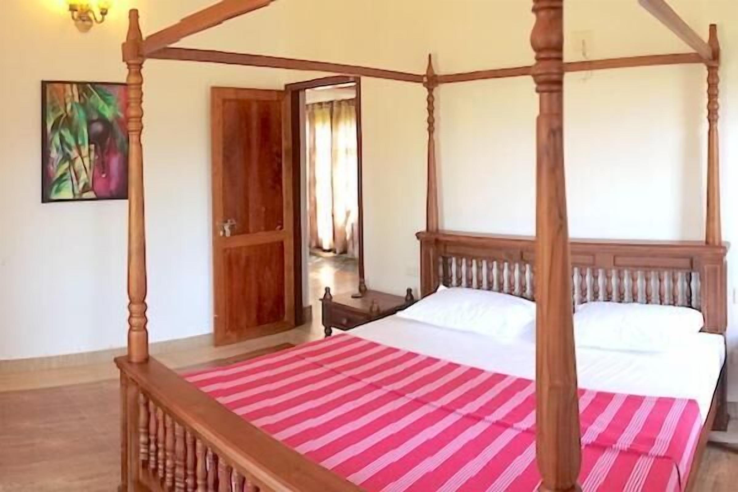 A four-poster bed with a red and white striped bedspread, a wooden headboard, and a nightstand with a lamp.