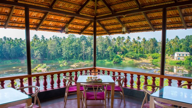 A covered outdoor seating area with a table and chairs, overlooking a river and dense greenery. - Rasa Gurukul (Chalakudy)
