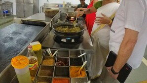A kitchen with stainless steel appliances, a large pot on a stove, and a spice rack with various spices. - Rasa Gurukul (Chalakudy)