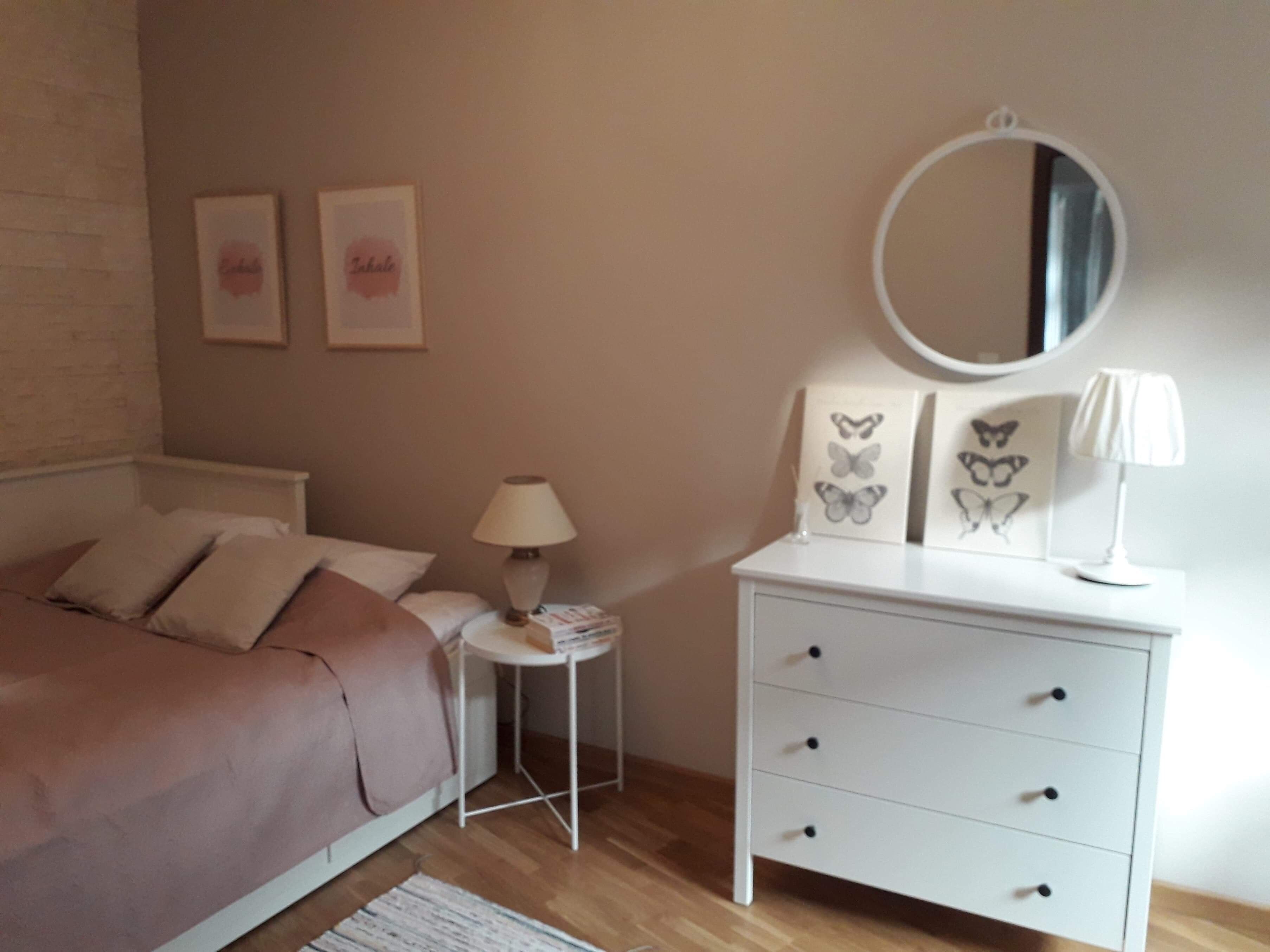 Une chambre à coucher comprenant un lit, une table de chevet, une lampe, une commode et des œuvres d’art murales.
