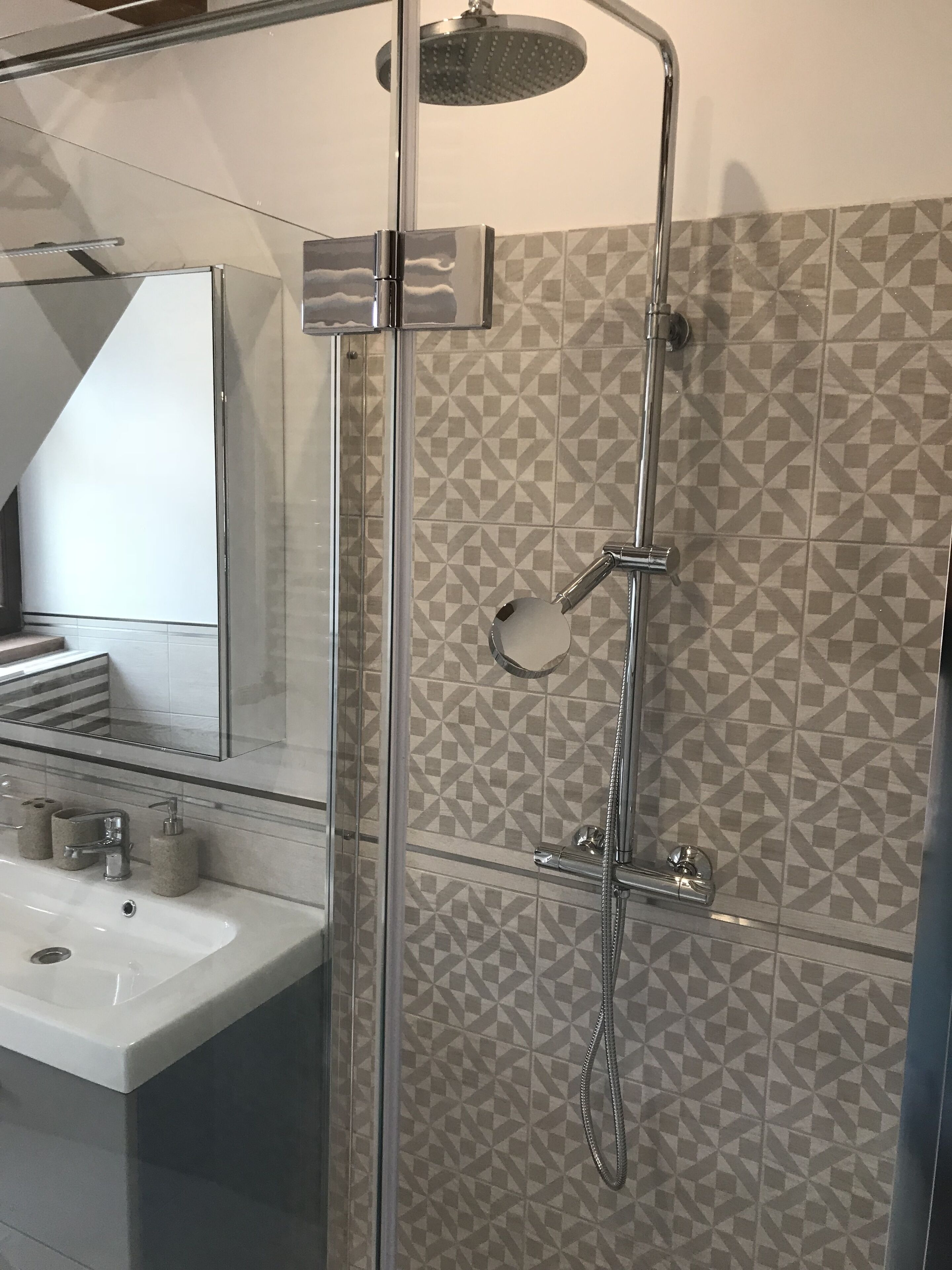 A modern bathroom with a glass-enclosed shower, a sink with a mirror, and patterned tiles.