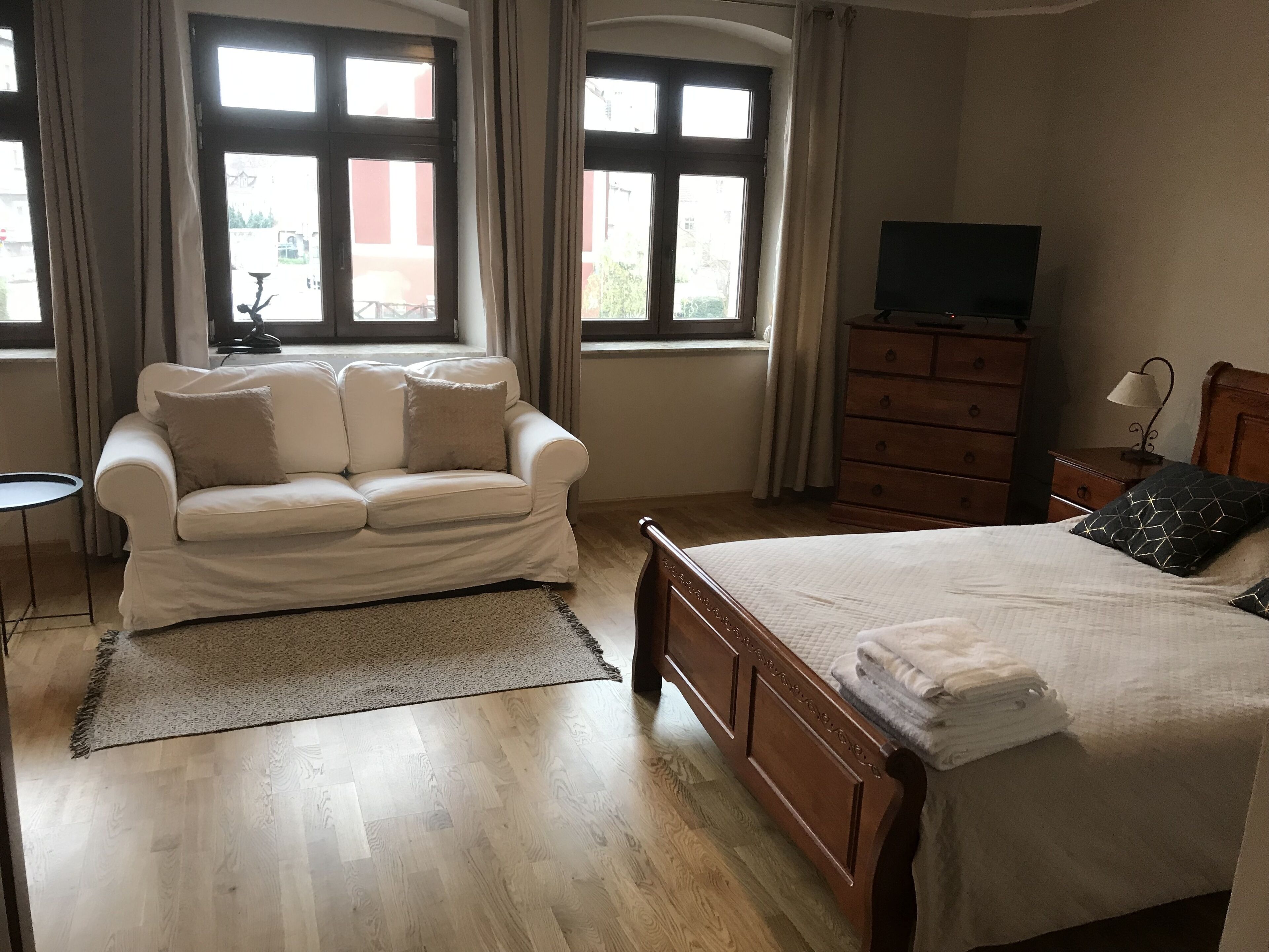 Un dormitorio con cama de madera, un sofá blanco, un televisor y un aparador.