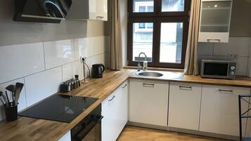 A modern kitchen with white cabinets, a wooden countertop, a built-in oven, a microwave, and a window with curtains.
