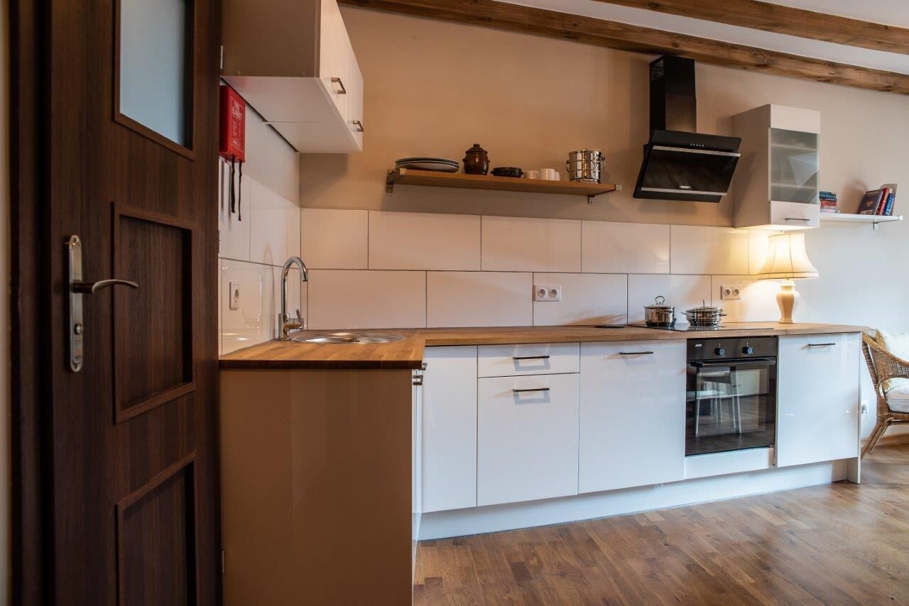 A modern kitchen with white cabinetry, a wooden countertop, a built-in oven, and a hanging pot rack.