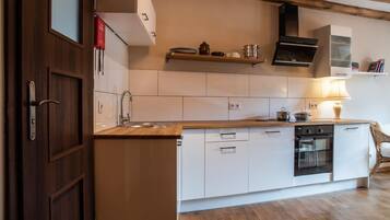 A modern kitchen with white cabinetry, a wooden countertop, a built-in oven, and a hanging pot rack.