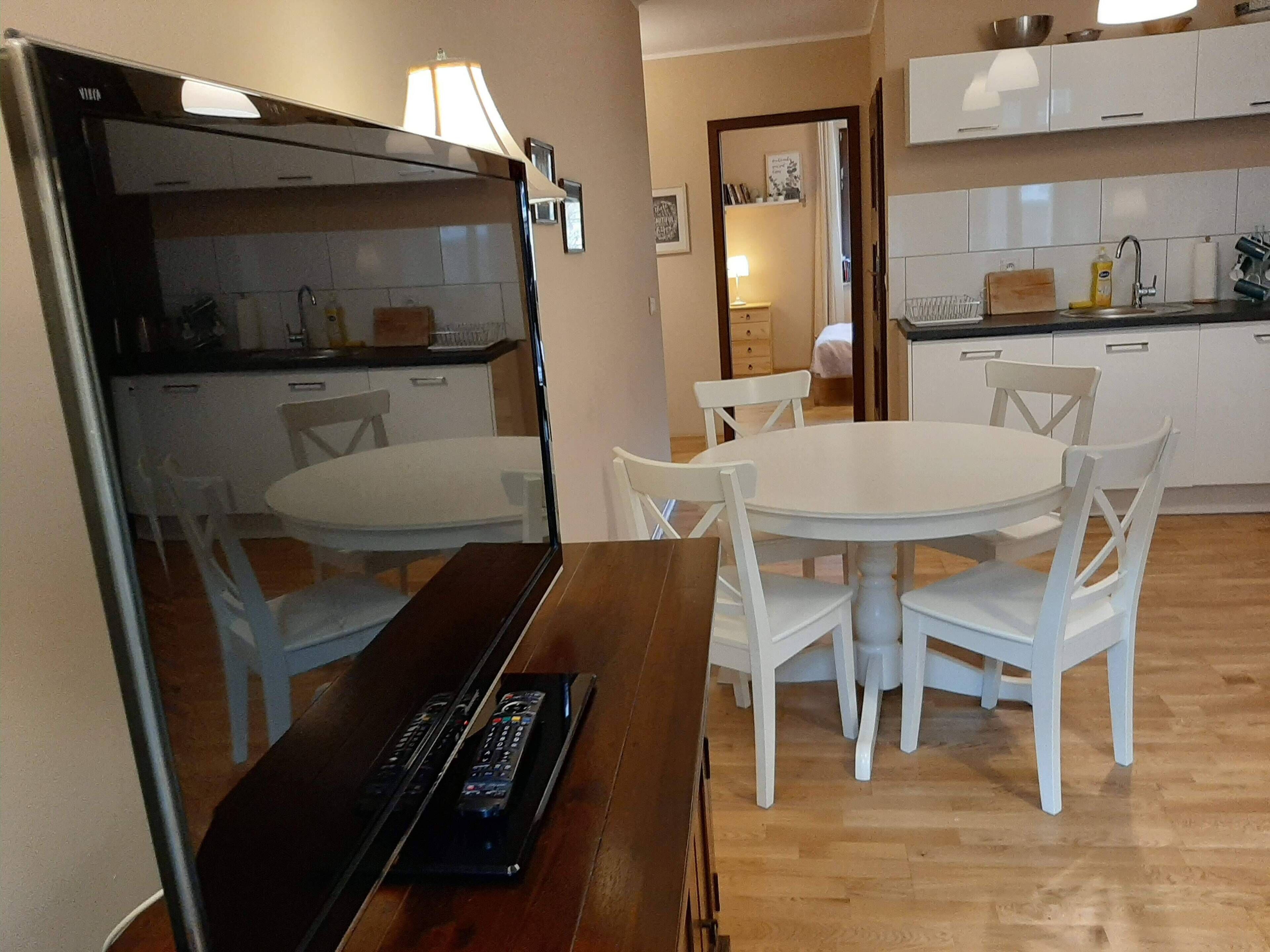 Ein Essbereich mit rundem Tisch und weißen Stühlen, eine Küche mit weißen Schränken und einem Kühlschrank.
