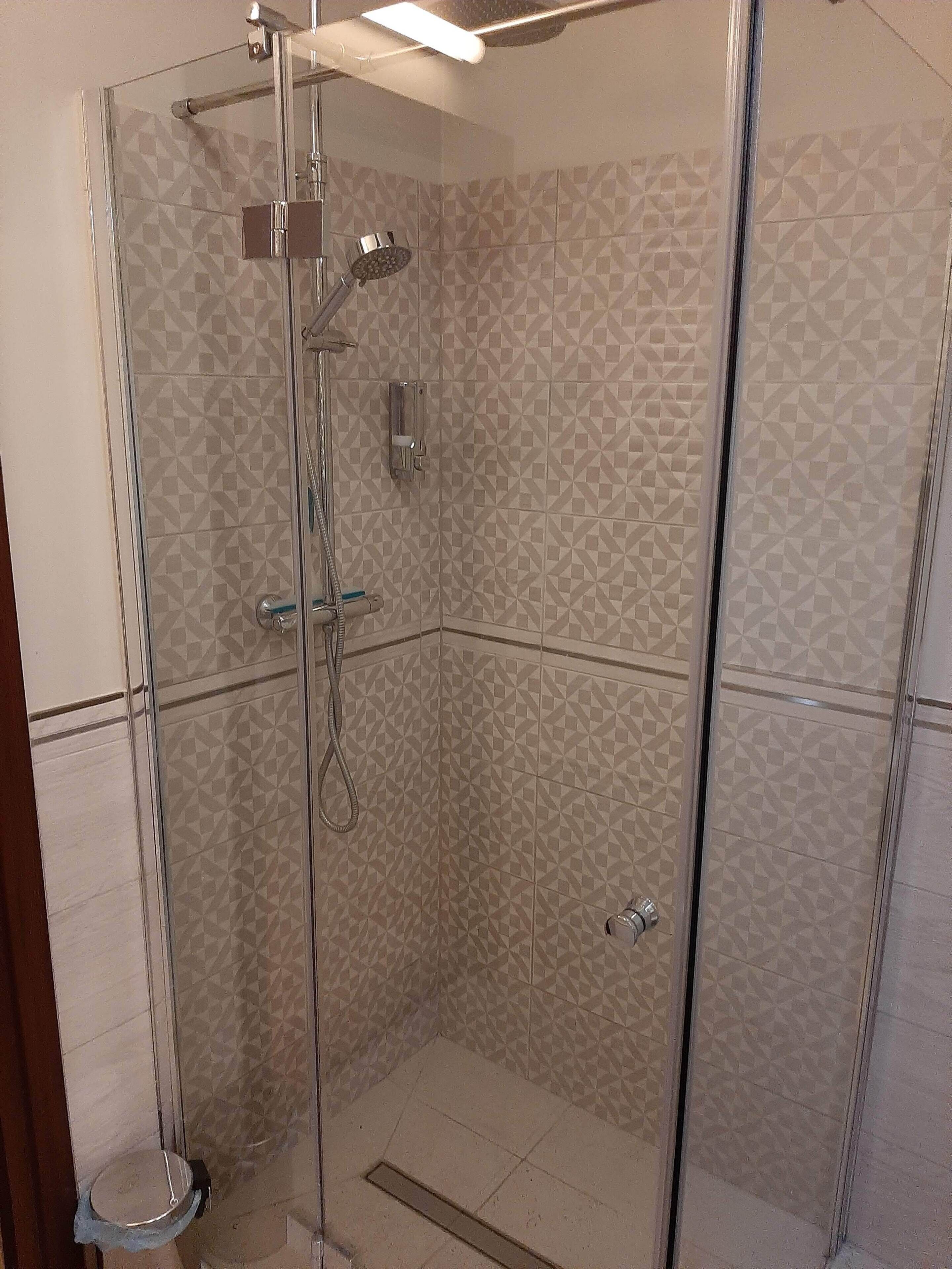 A glass-enclosed shower with a geometric tile pattern on the walls and floor.