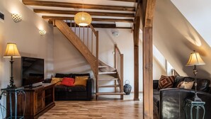 Un espacio habitable tipo loft con vigas de madera a la vista, una escalera de madera y un sofá de cuero negro.
