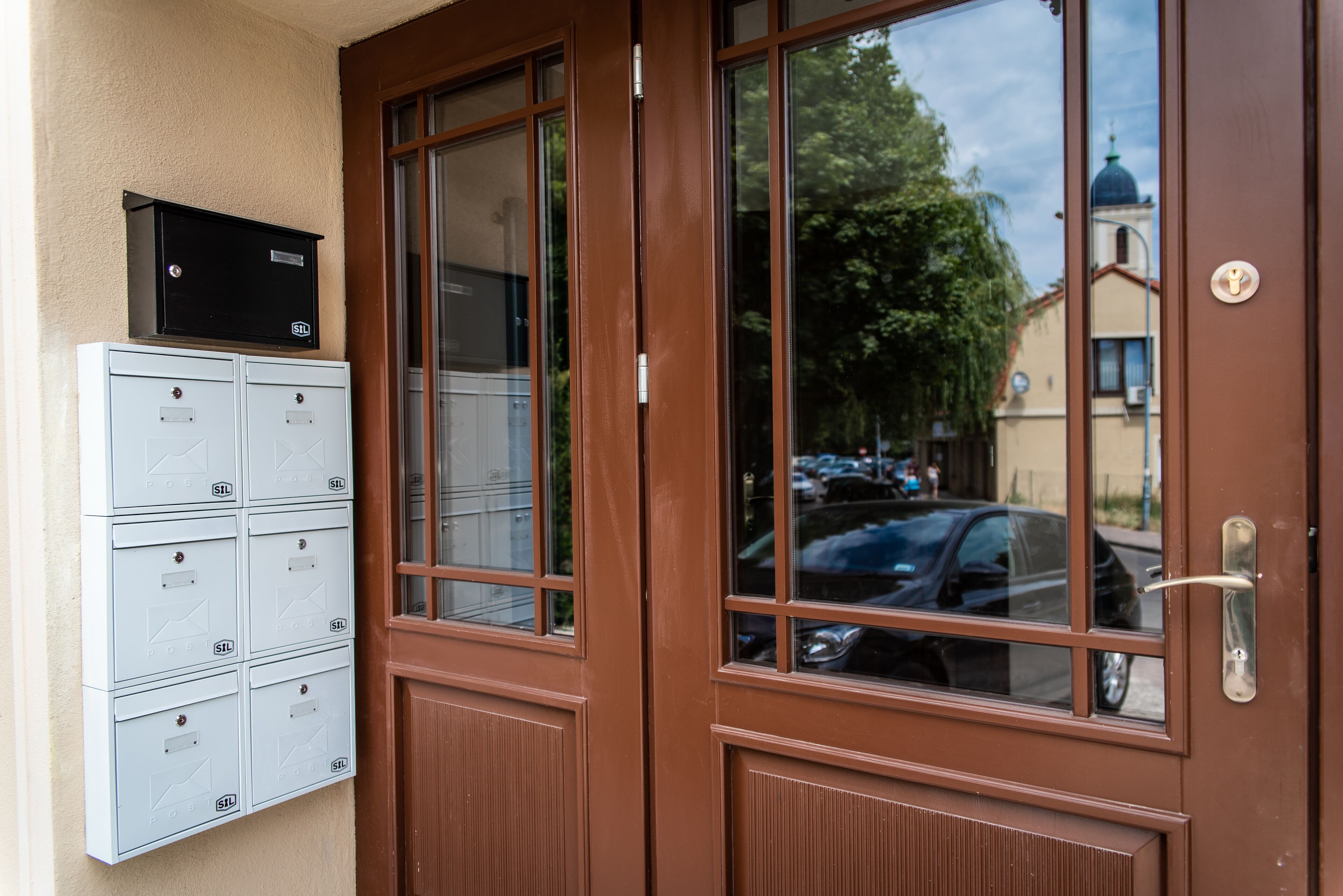 A brown door with a window, a mailbox, and a black box on the wall.