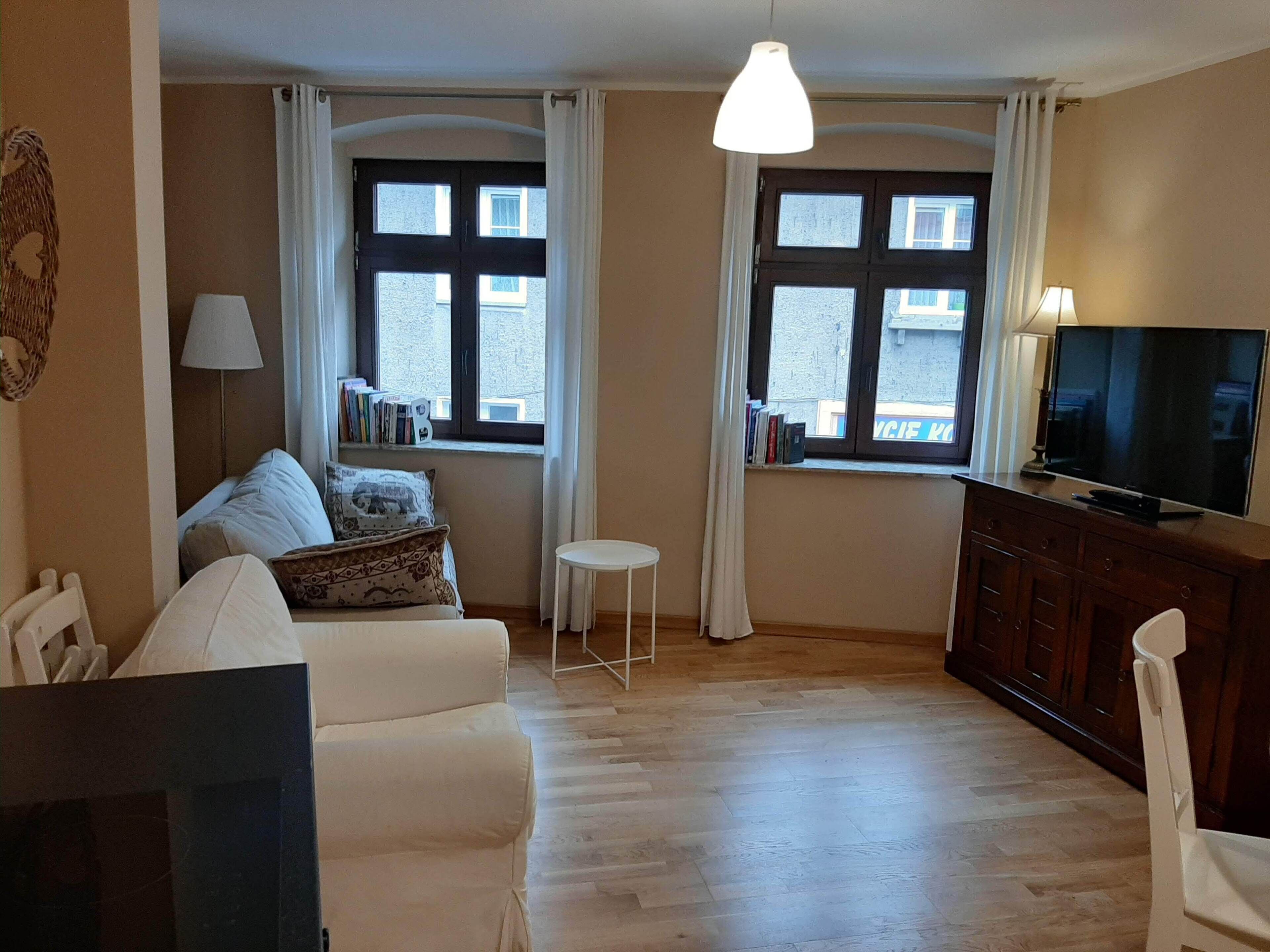 A living room with a sofa, a small table, a TV, and two windows with curtains.