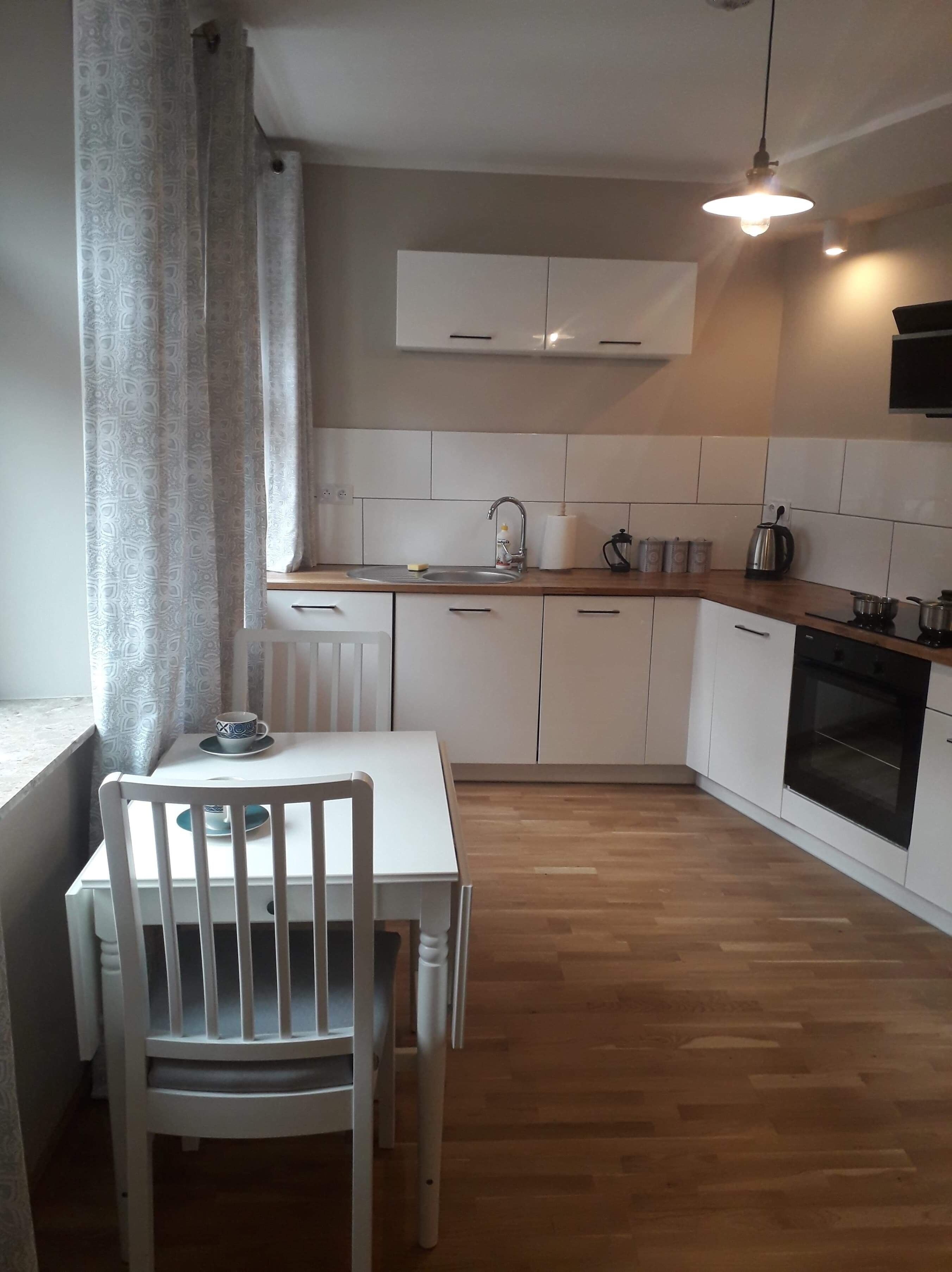 A compact kitchen with white cabinets, a wooden countertop, a built-in oven, and a window with curtains.