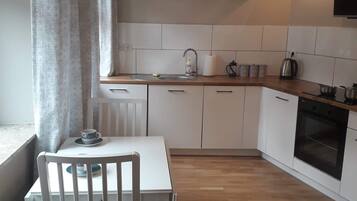A compact kitchen with white cabinets, a wooden countertop, a built-in oven, and a window with curtains.