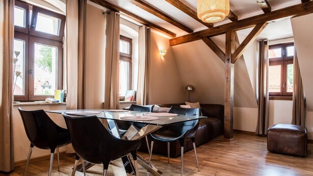 Un comedor con una mesa de vidrio, sillas negras y techo de madera.