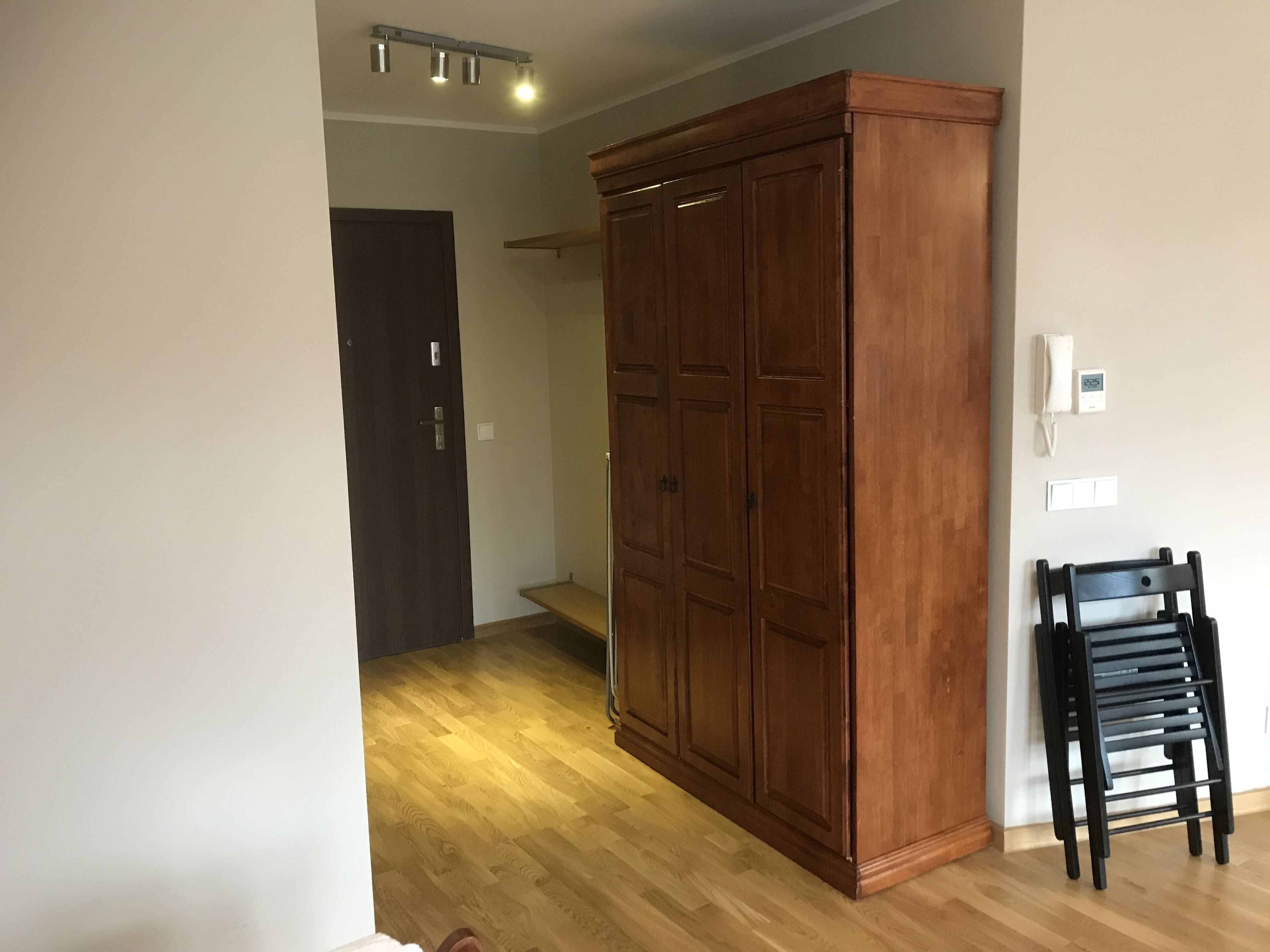 Une pièce avec une armoire en bois, une chaise noire et une porte qui donne sur une autre pièce.
