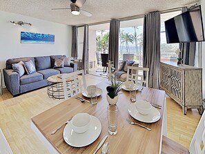 Ein modernes Wohnzimmer mit einer Couch, einem Esstisch für zwei Personen und einem an der Wand befestigten Fernseher.