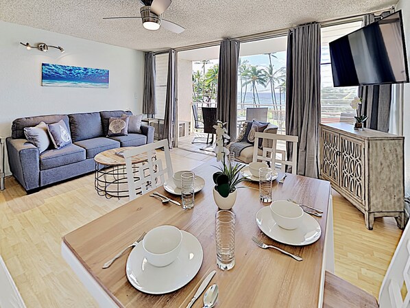 A modern living room with a sofa, dining table set for two, and a TV mounted on the wall.