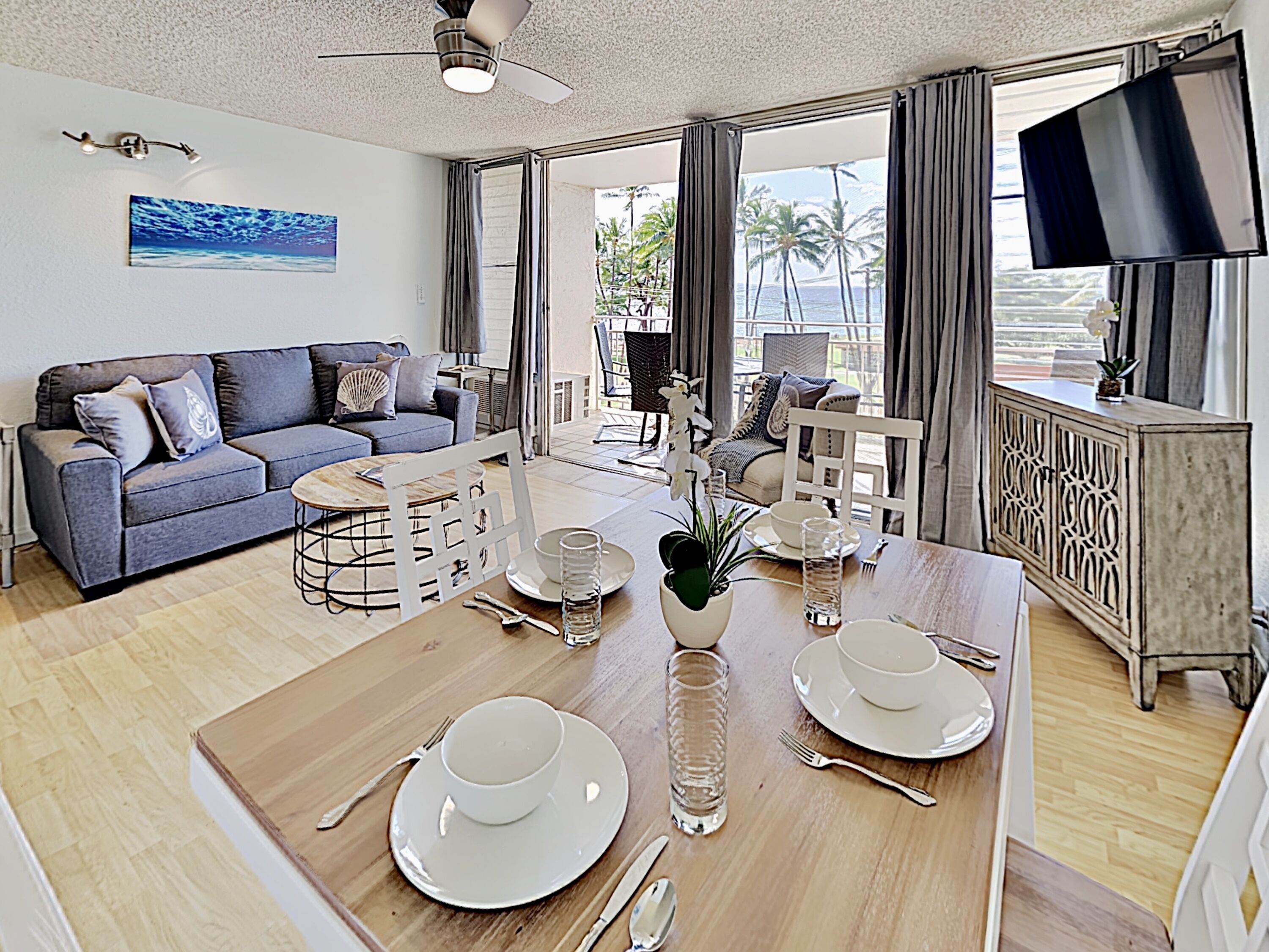 A modern living room with a sofa, dining table set for two, and a TV mounted on the wall.