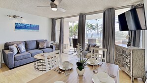 Un salon moderne avec un canapé, une table à manger pour deux personnes et un téléviseur fixé au mur.