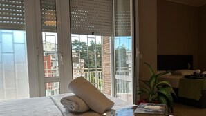 Habitación de hotel con una cama, una toalla enrollada, un libro y una planta.