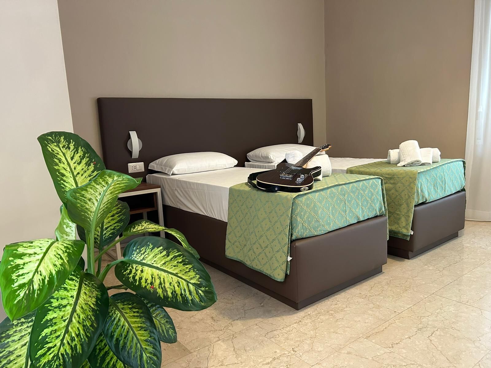Habitación de hotel con dos camas, una guitarra, toallas y una planta grande.