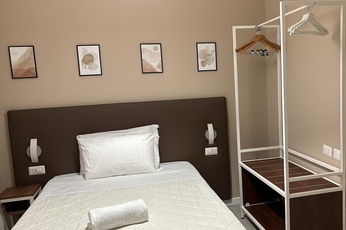 A bedroom with a bed, a bedside table, a wardrobe with a mirror, and wall-mounted artwork.