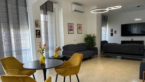 Una sala de estar moderna con un sofá, un televisor y un comedor con sillas amarillas y una mesa.