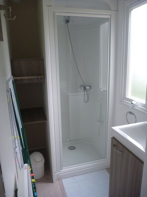 A bathroom with a glass-enclosed shower, a white sink, and a window.