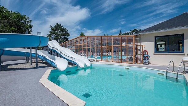 Una piscina con dos toboganes, una zona de estar cubierta y un edificio con grandes ventanales.