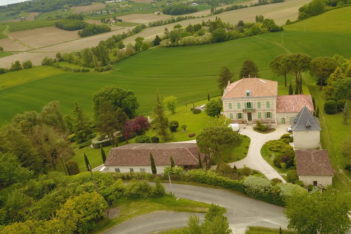 Vista aérea de una extensa propiedad con una casa principal, un edificio más pequeño y amplios campos verdes.