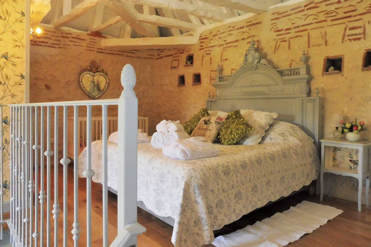 Un dormitorio con una cama, una mesita de noche, una barandilla blanca y suelo de madera.