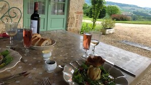Una mesa de comedor dispuesta con copas de vino, pan y un bol de ensalada, con vistas a un paisaje pintoresco.