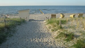 Een zandstrand met een houten tuinhuisje, meerdere strandstoelen en een houten omheining langs het water.