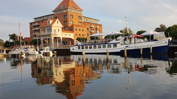 Een gebouw aan het water met meerdere verdiepingen, een boot afgemeerd in de buurt, en spiegelingen op het water.