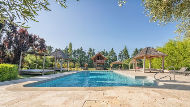 A swimming pool with lounge chairs and gazebos, surrounded by trees and a wooden structure in the background. - Near L'Isle-sur-la-Sorgue, quiet old Provençal Mas, 19 Pers. Swimming pool. (Le Thor)